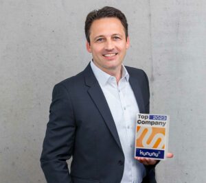 Gründer Sven Scholz hält die Auszeichnung "Top Company 2023" in der Hand und lächelt