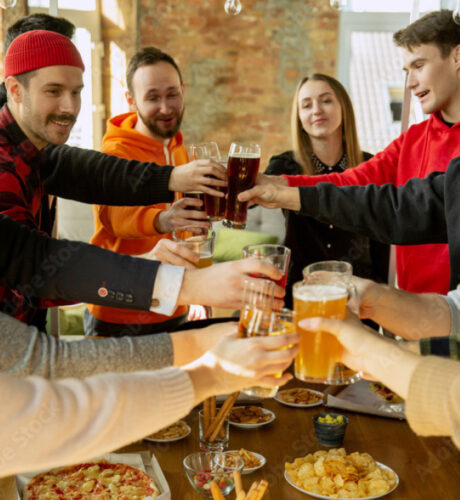 Eine Gruppe von Menschen stößt in zwangloser Innenatmosphäre an einem Tisch mit verschiedenen Snacks und Getränken an.