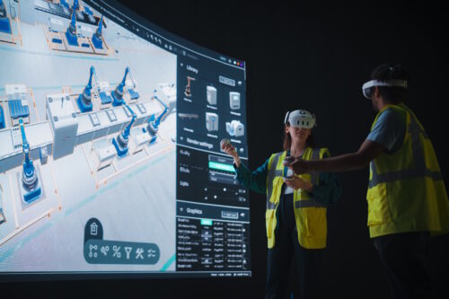 Zwei Personen in Sicherheitswesten und VR-Headsets interagieren mit einem großen virtuellen Bildschirm, der ein digitales Modell einer Industrieanlage zeigt.